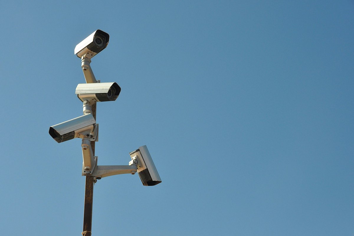 A group of surveillance cameras are mounted in different directions on a single pole against a clear blue sky.