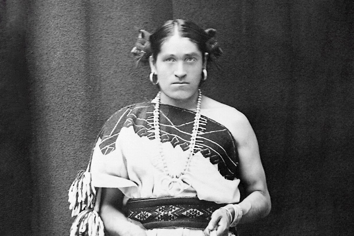 A black and white portrait of Zuni two-spirit person We'wha, wearing a traditional knee-length manta dress fastened over the right shoulder.