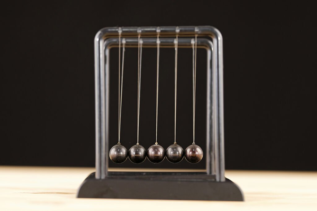 A newton’s cradle with five swinging balls in near-balance.