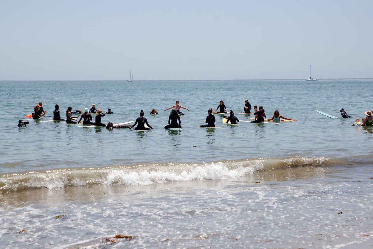 A group of a dozen people on paddleboards in the ocean, arranged in a circle.