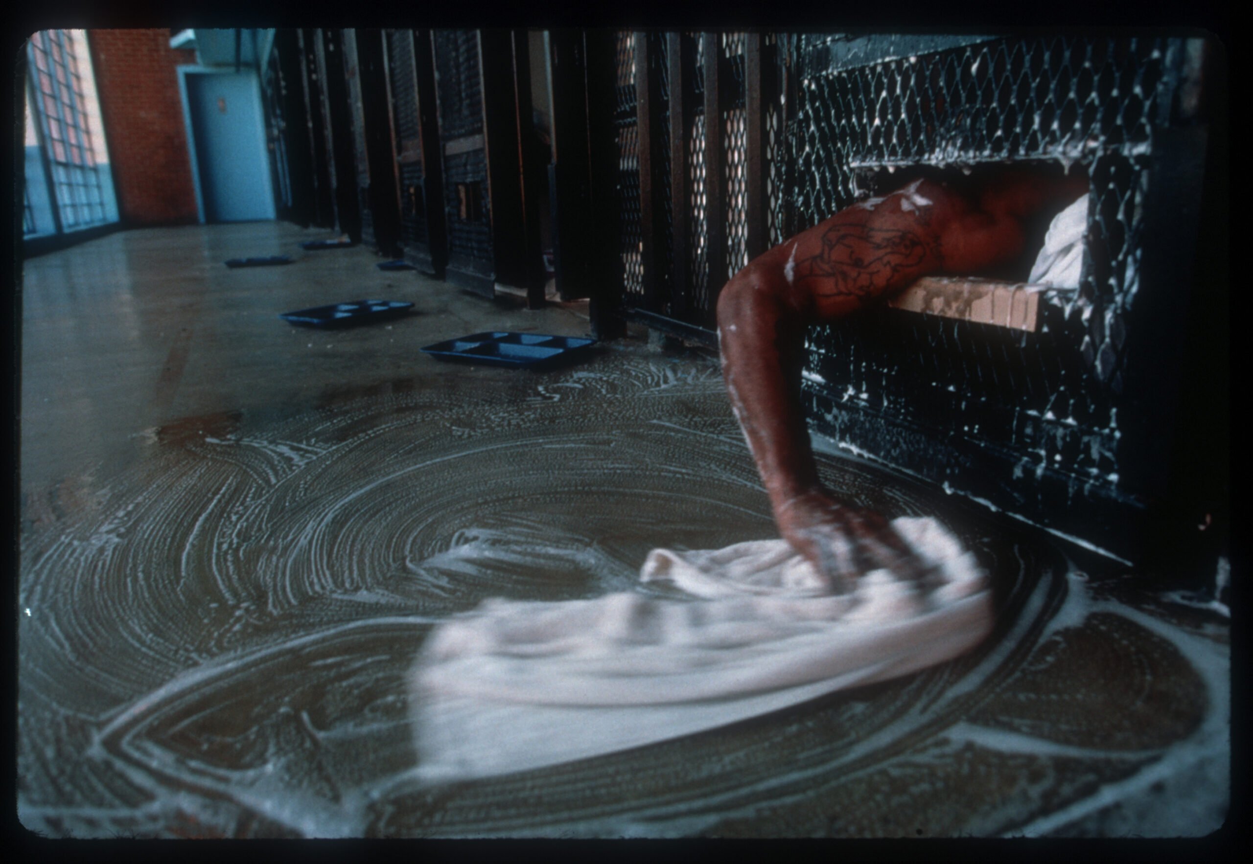 A prisoner in Beaumont, TX attempts to clean up the area around his cell after it was flooded with sewage from the tier above. Stopping up toilets in the cells is a form of protest in prison. (Photo by Andrew Lichtenstein)