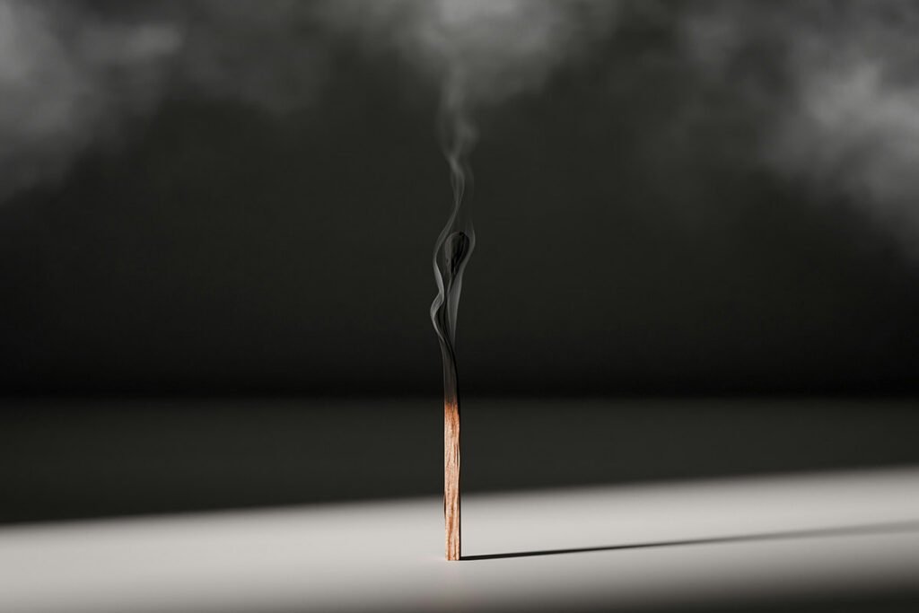 A single smoking match, recently extinguised propped on a dramatically lit surface, casting a long shadow.