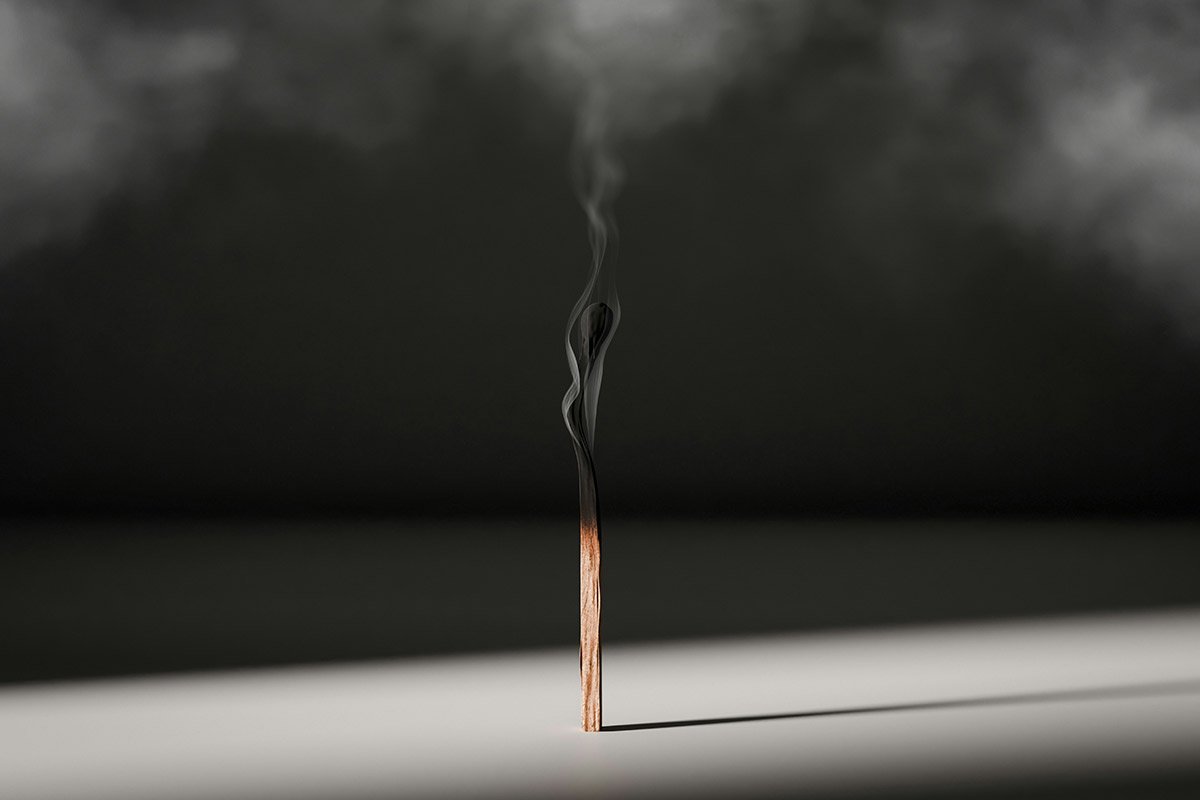 A single smoking match, recently extinguised propped on a dramatically lit surface, casting a long shadow.