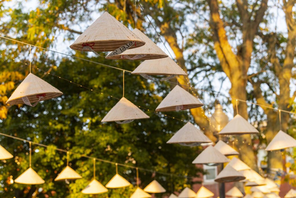 A closeup of conical hats hanging from a line overhead. Journey of Light: A 1975 Memory Field, temporary installation by Ngoc-Tran Vu, 2025.