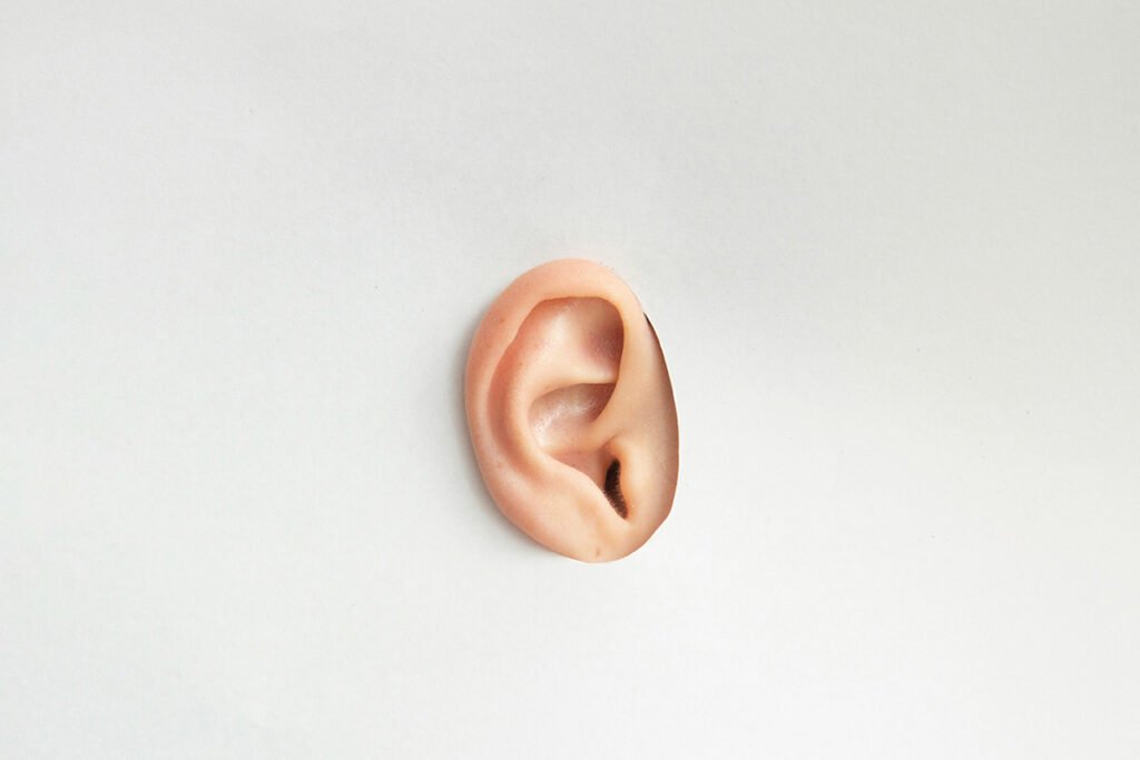 A person’s ear exposed through a hole cut into a white sheet of paper.