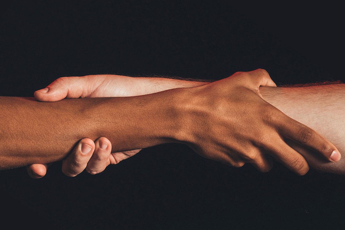 Two hands–one Black and one white–grasping each other at the wrists in partnership and trust.