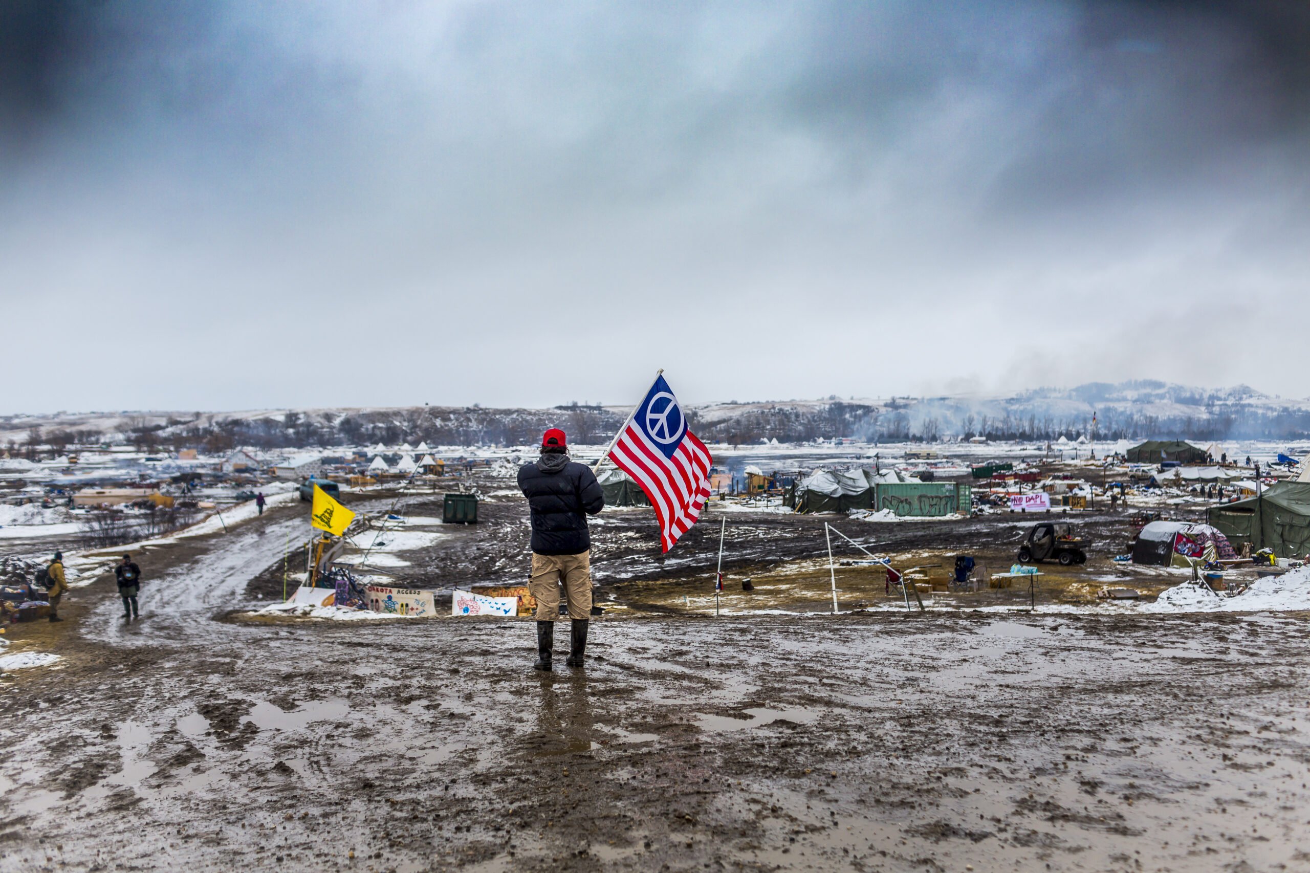 STANDING ROCK, NORTH DAKOTA - FEBRUARY 22, 2017: A lone Water Protector holds a flag while looking out on the Standing Rock encampment, hours before the camp was slated to be raided by militarized law enforcement and the National Guard on February 22, 2017, in Standing Rock, North Dakota. In April of 2016, members of the Standing Rock Sioux tribe began protesting the construction of the Dakota Access Pipeline (DAPL), the 3.7 billion dollar underground oil pipeline stretching 1,172 miles from the Bakken shale oil fields in northwest North Dakota to an oil terminal in Patoka, Illinois.