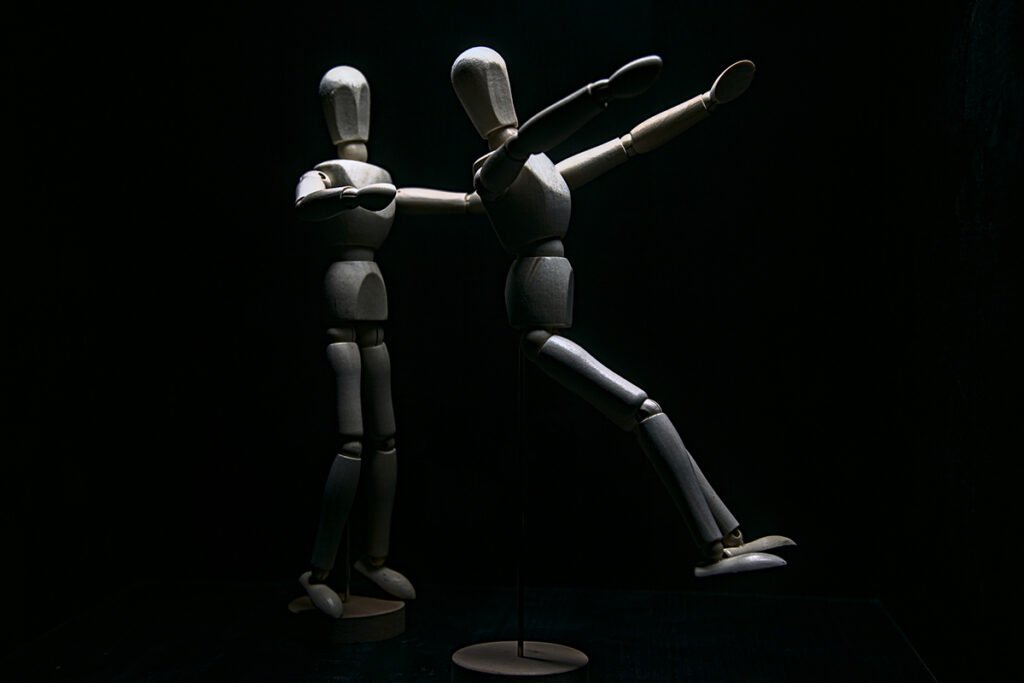 Two wooden mannequins performing a trust fall, where one falls backwards and the other outstretches its arms to catch the falling one.