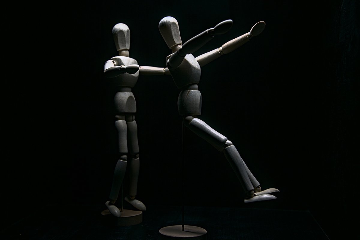 Two wooden mannequins performing a trust fall, where one falls backwards and the other outstretches its arms to catch the falling one.