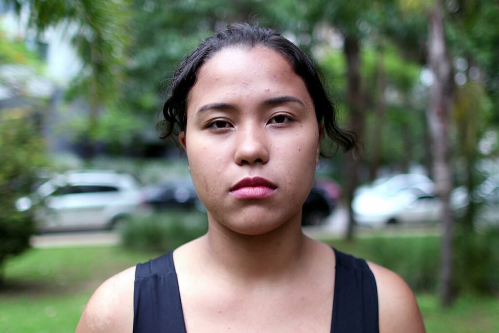 A young Latino woman stands outside and faces towards the camera with a determined look on her face.