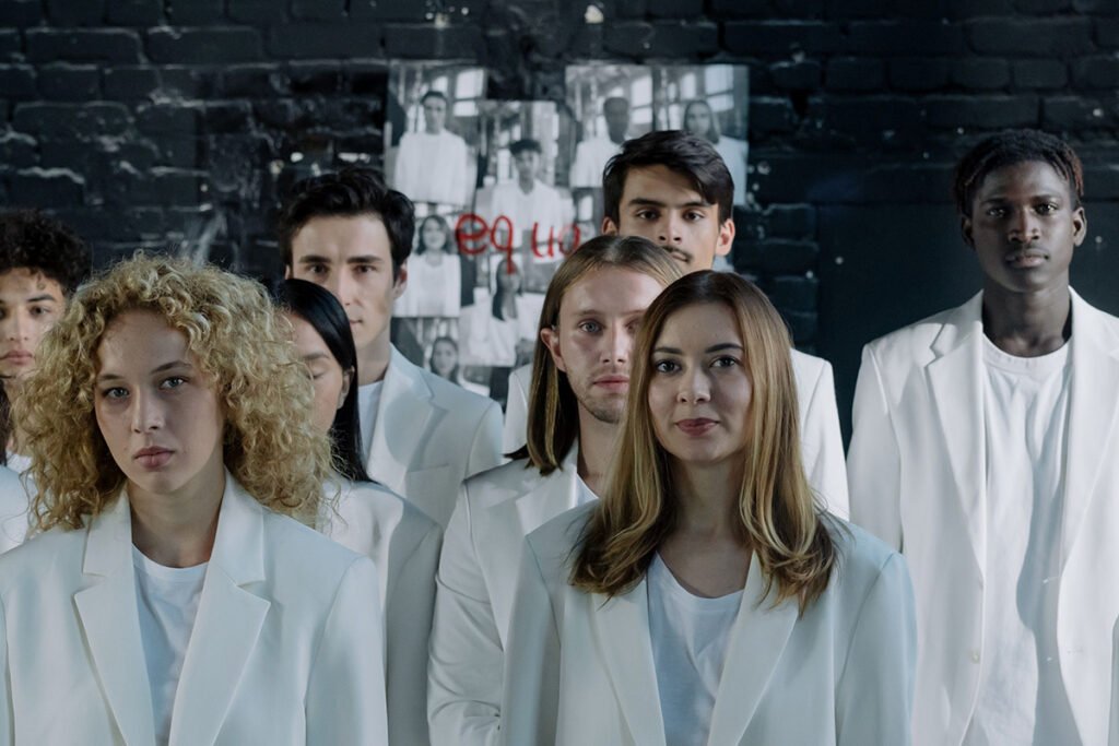 A group of many, diverse young adults wearing white suits and facing the camera with serious looks on their faces.