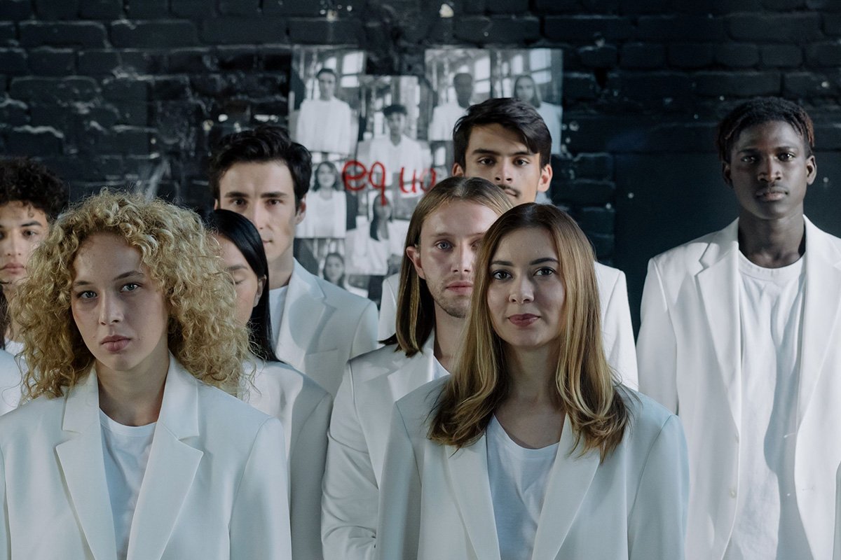 A group of many, diverse young adults wearing white suits and facing the camera with serious looks on their faces.