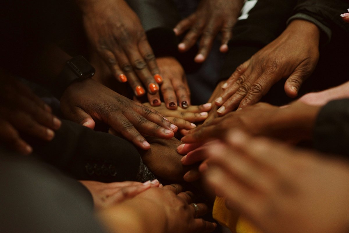 Many Black people reach their hands together, touching each other gently in support and community.