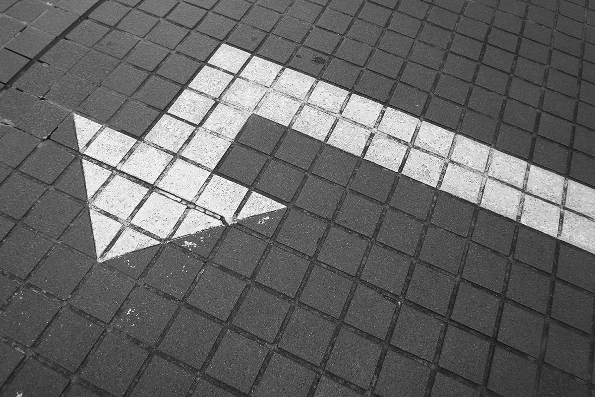 An arrow painted onto a paved sidewalk. The arrow is painted to sharply change direction.