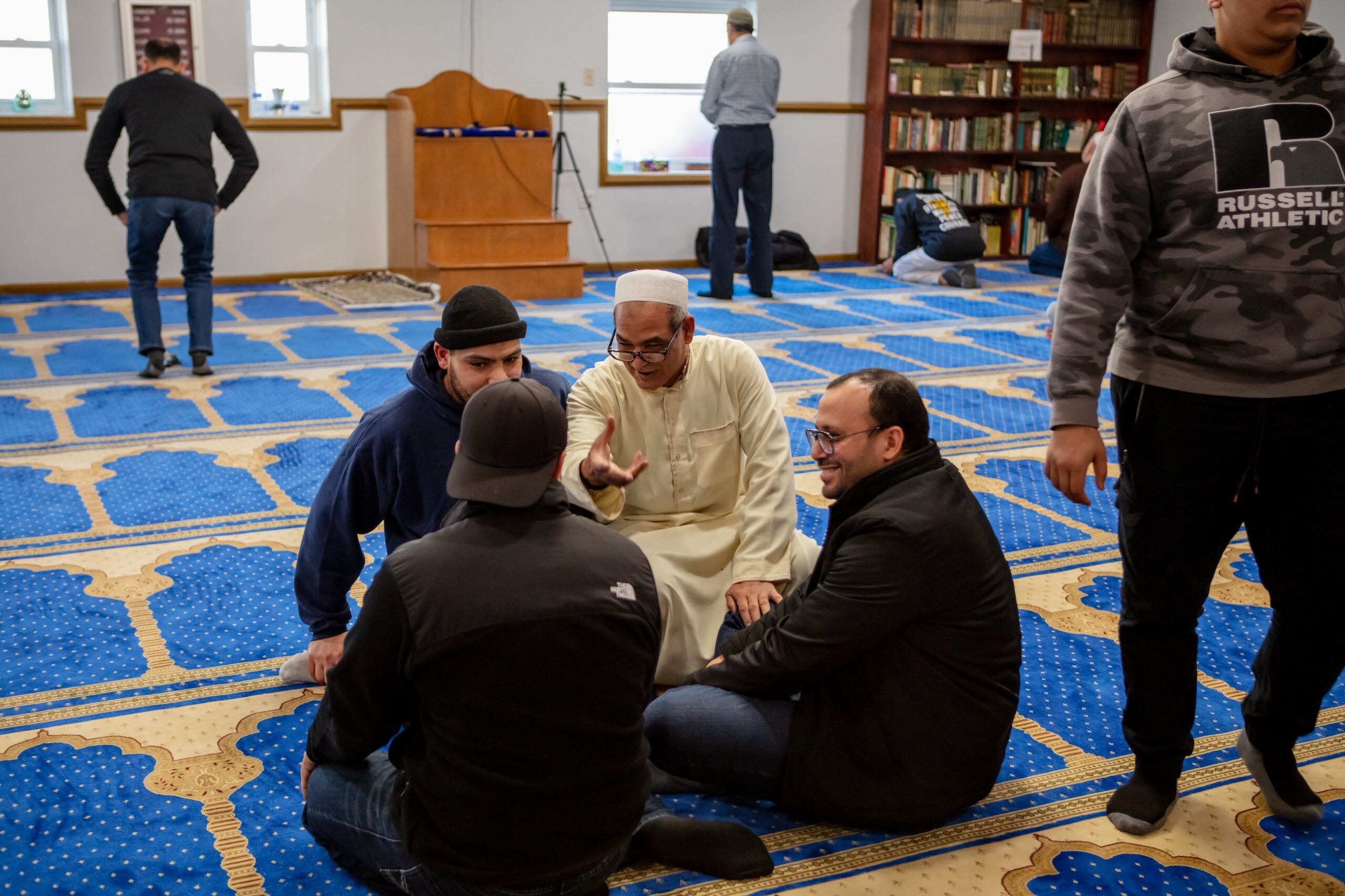 After Jummah conversation | American Muslim Experience documentaryImam in the beige thobe, speaking to a few of the Friday prayer attendees. Members of this small masjid are like a close-knit family, sharing life updates. Photography by Syed Yaqeen.