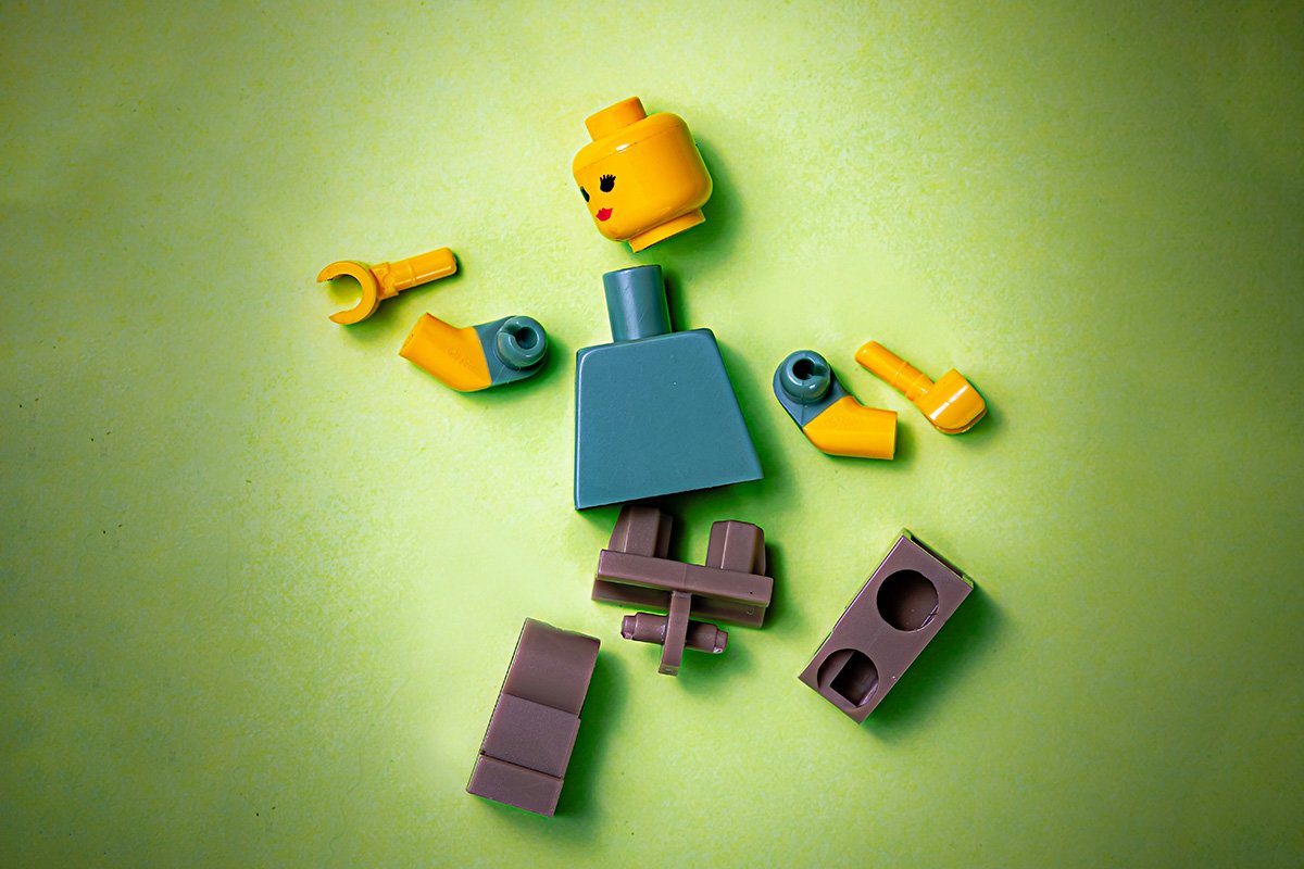 A lego figure broken apart into several pieces and scattered across a green background.