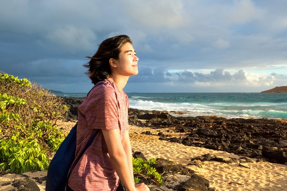 A young Native Hawaiian woman sitting on rocky beach watching the sunrise.
