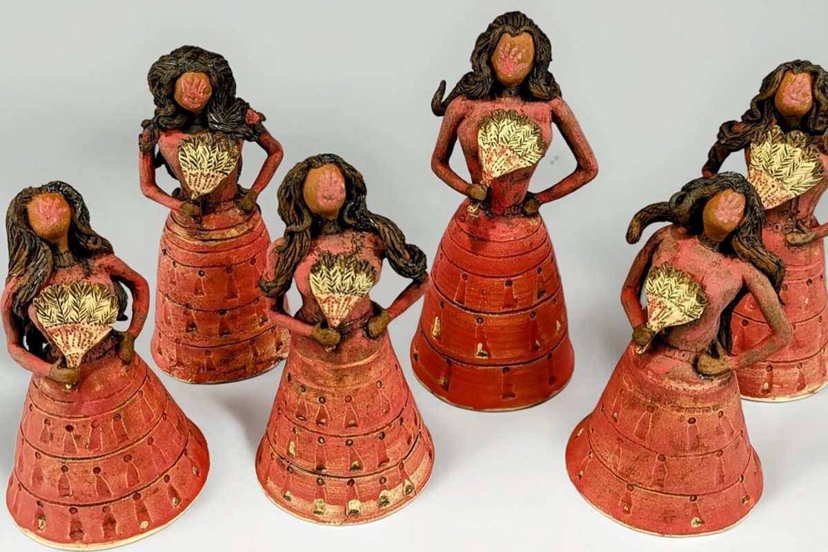 Clay figurines of brown women with long hair and ong red dresses, holding eagle feather fans. They have a red handprint on their featureless faces.