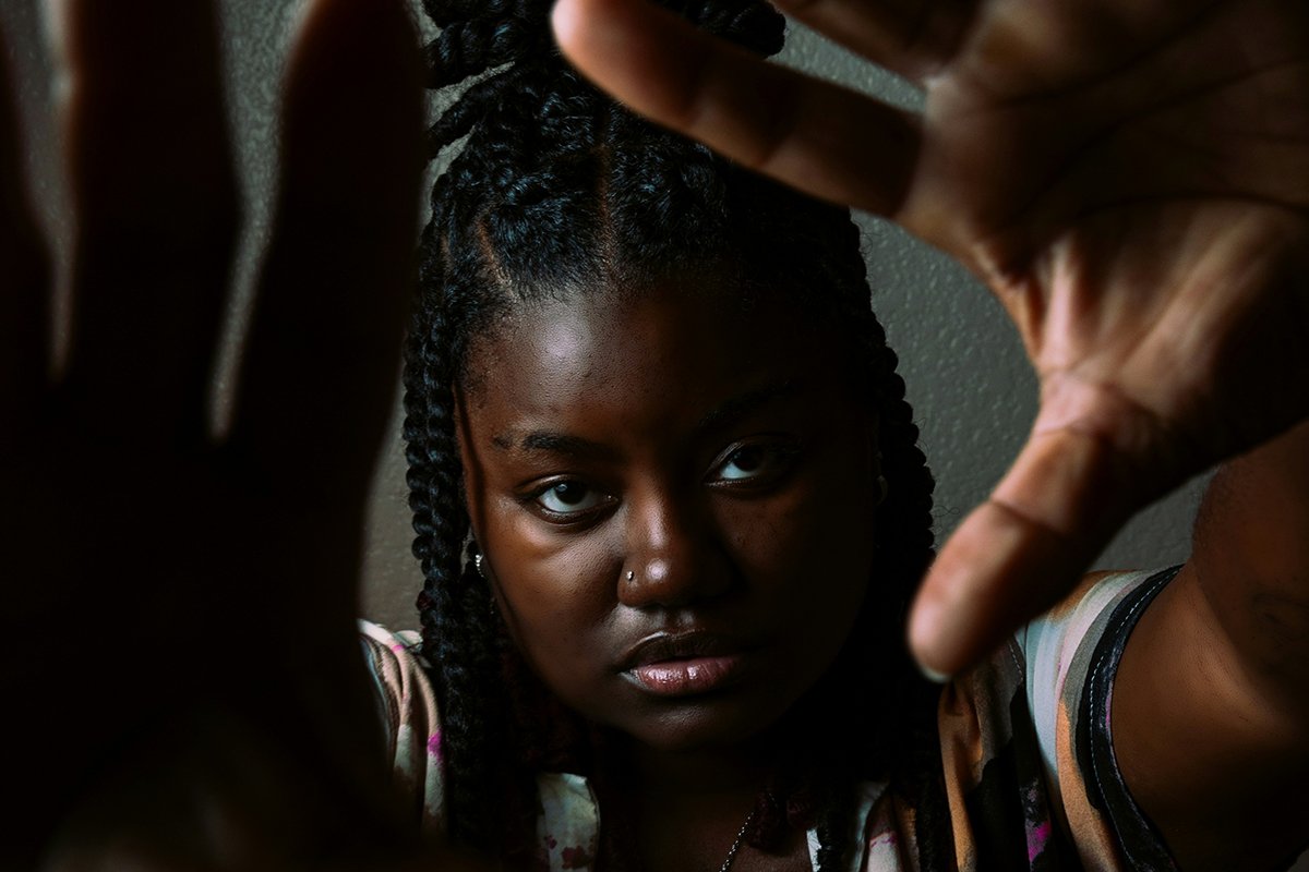 A Black woman with braids and a serious expression holds up her hands to the camera, as if to frame something in front of her.