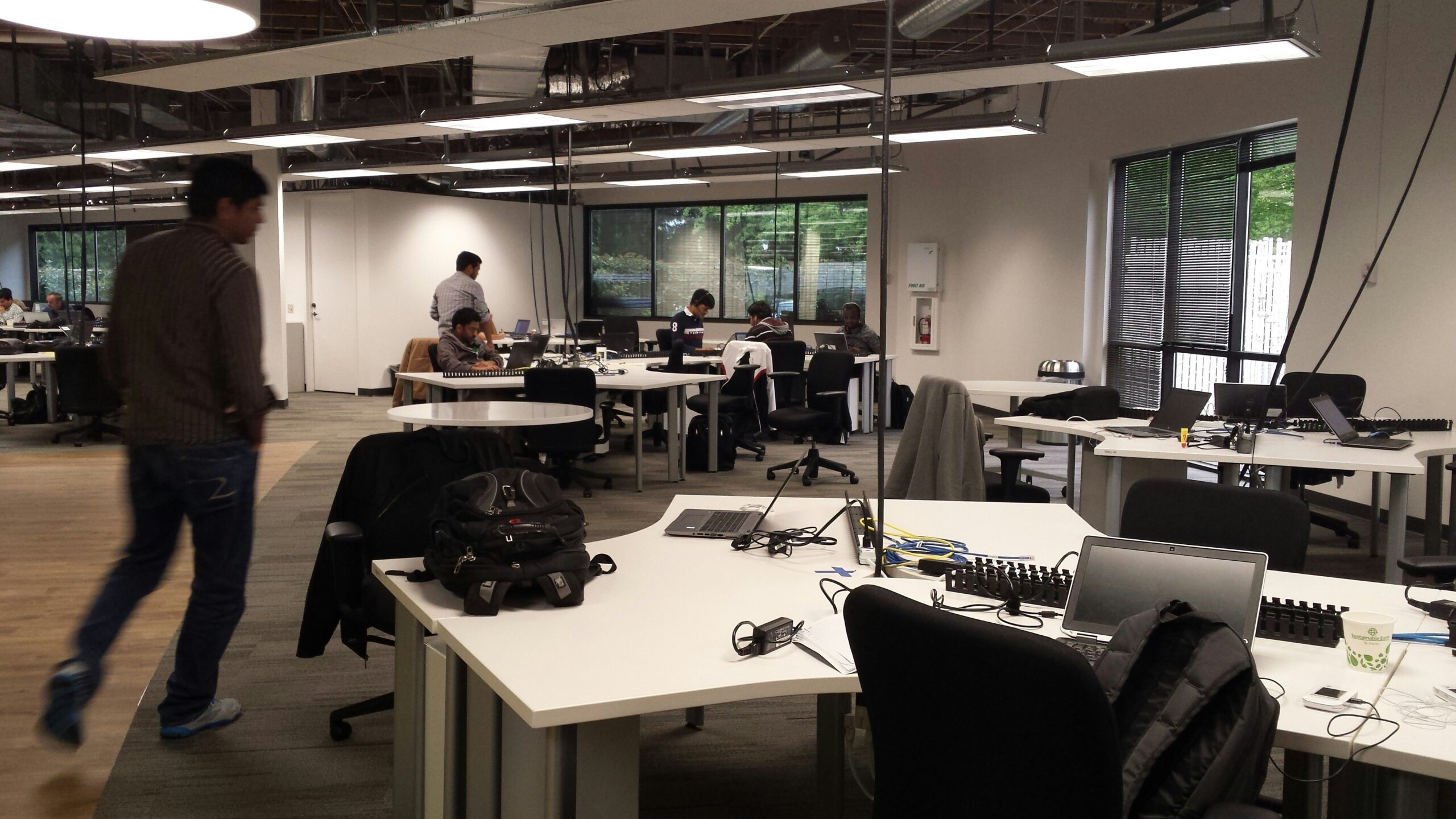 Office workers walk through a contemporary open office, with empty desks around the space.