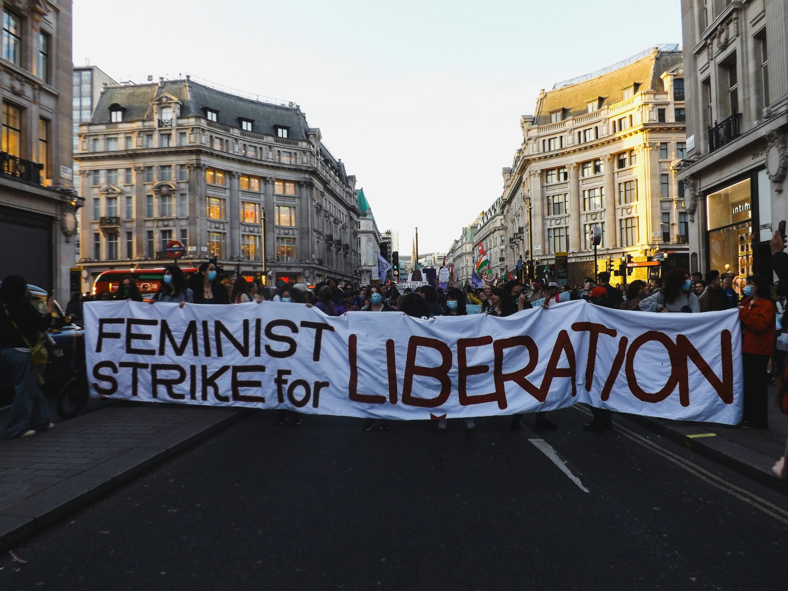 People carrying a banner that reads "Feminist Strike for Liberation" in a street with buildings in the background during the Women's Day Walk 2025 in London