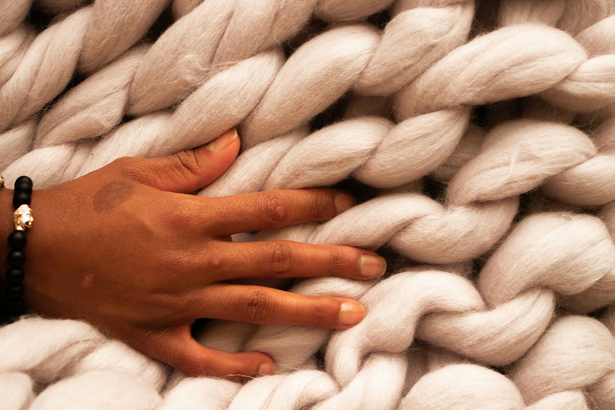 A Black person’s hand grazes a light-colored textile made from natural woolen fibers.