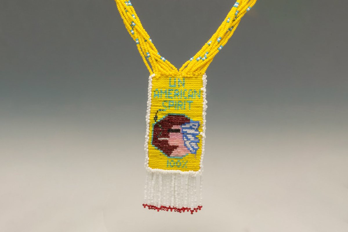 A yellow beaded necklace that says, “UnAmerican Spirit” and shows a Native man smoking a cigarette.