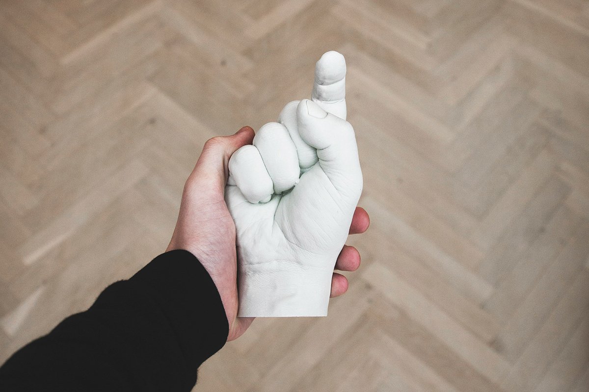 A white person’s hand holding a white plaster model of a hand pointing back at the viewer.