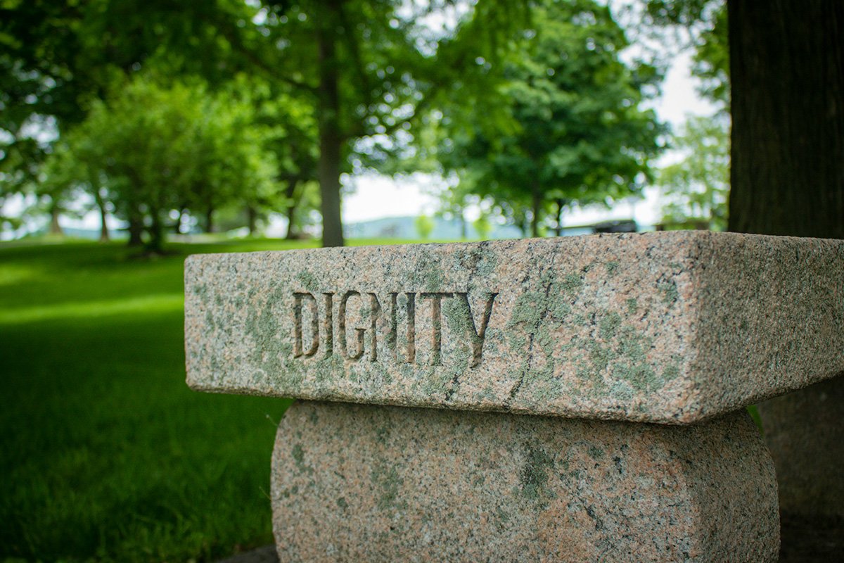 A stone pillar with the word “Dignity” carved into it in capital letters.