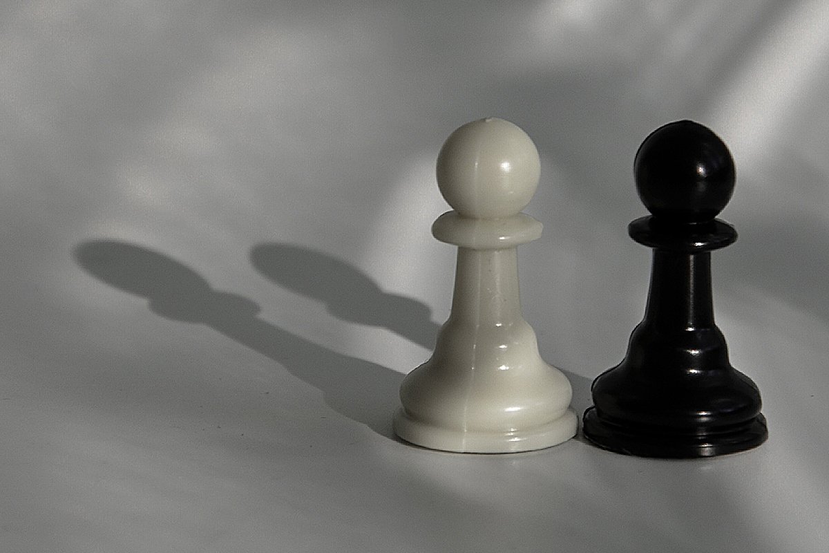 A white and black chess pawn placed next to each other, washed in soft light.