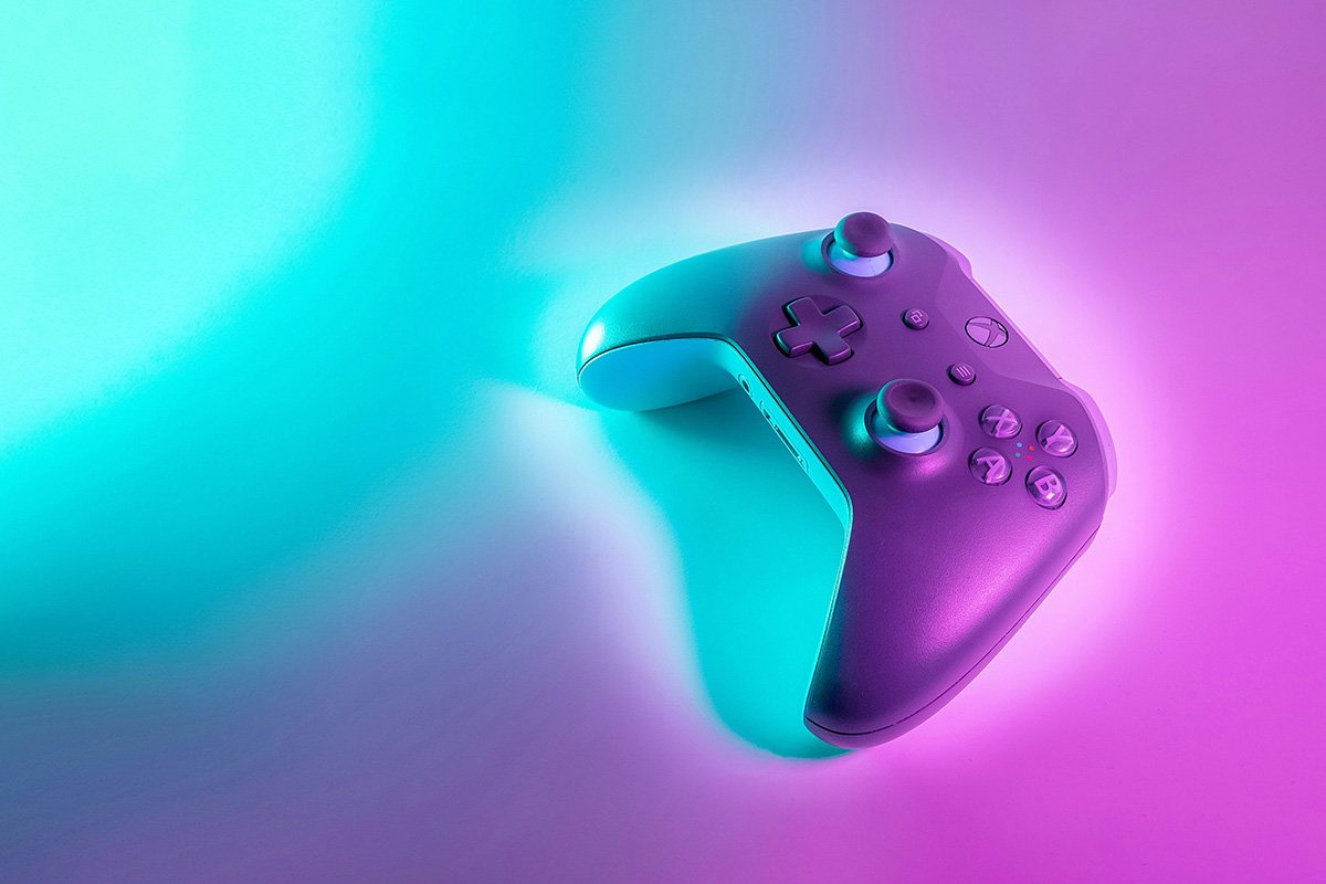 An X-box controller is placed at an angle against a surface lit with pink and blue lighting.