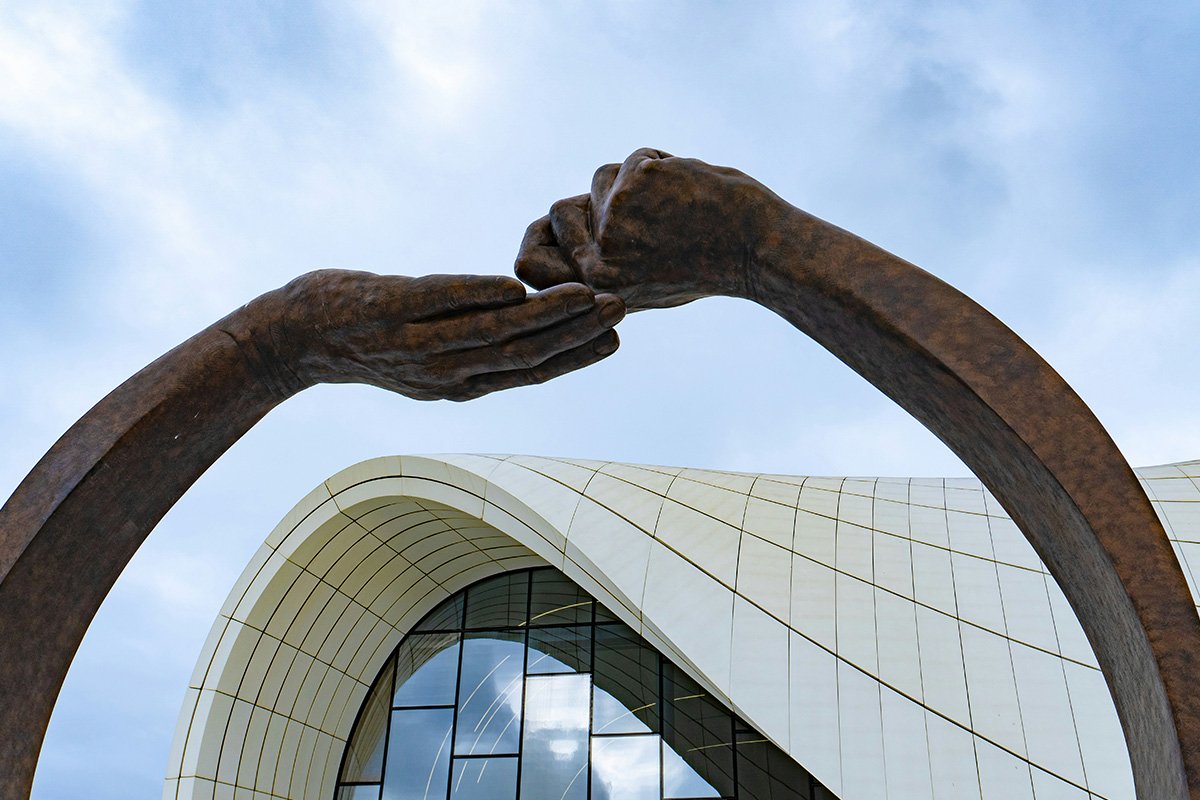 A bronze scuplture of two hands, one bends backgwards into a fist, and the other cradles the fisted hand.