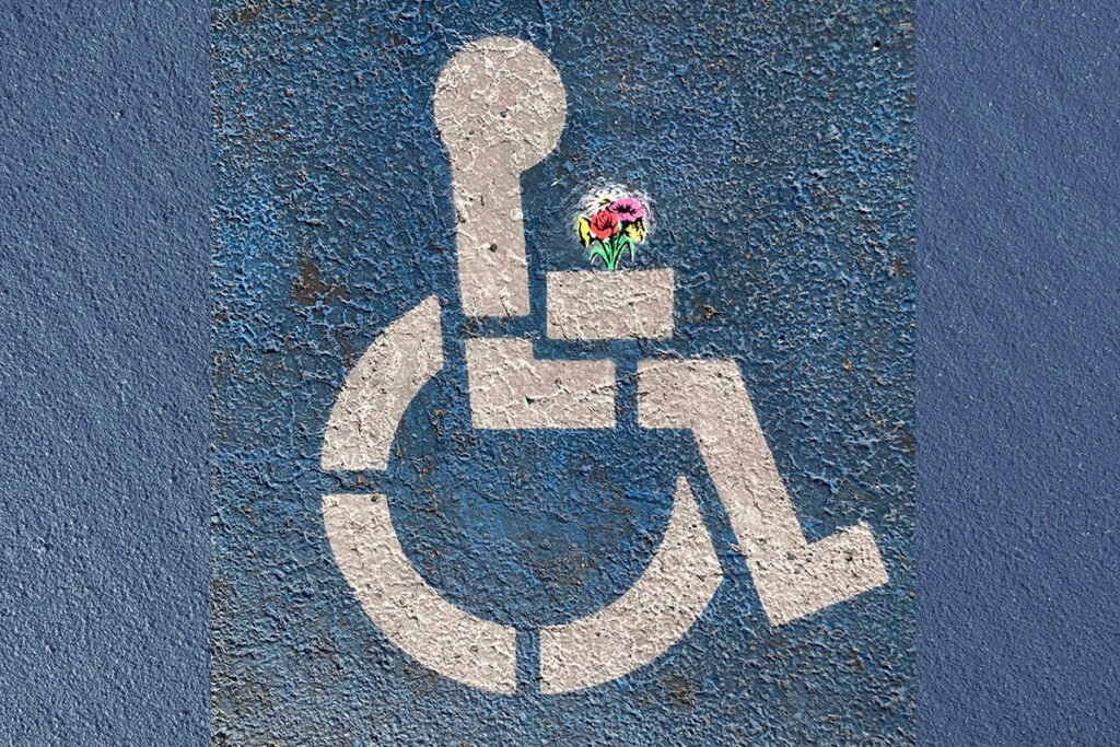 An International Symbol of Access (ISA) painted onto a blue textured background with a bouquet of flowers spraypainted in the symbol’s hands.