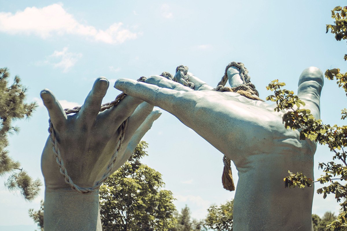 A stone sculpture of two hands raeaching backwards towards each other, while a rope intertwines between the two hands.