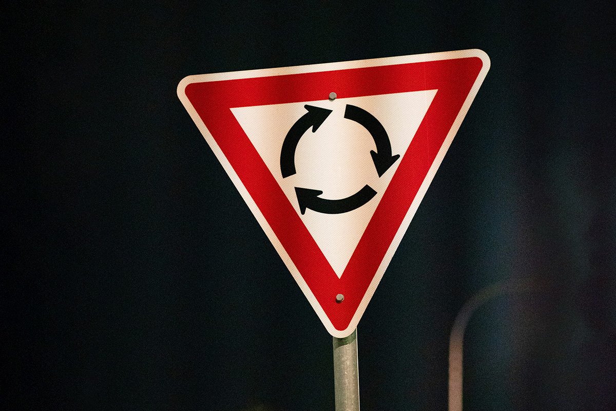 A road sign indicating a roundabout, with three black arrows circling a central point, pointing at each other.